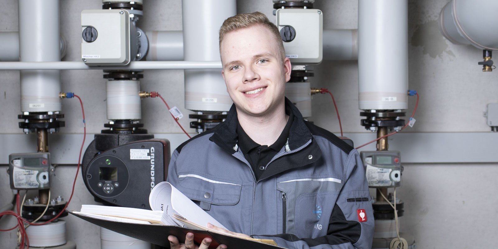 Ein junger Anlagenmechaniker der vor einer Heizungsanlage steht