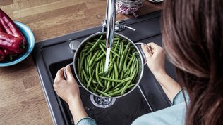 Ein Kochtopf mit Bohnen wird mit Wasser gefüllt in der Küchenspühle